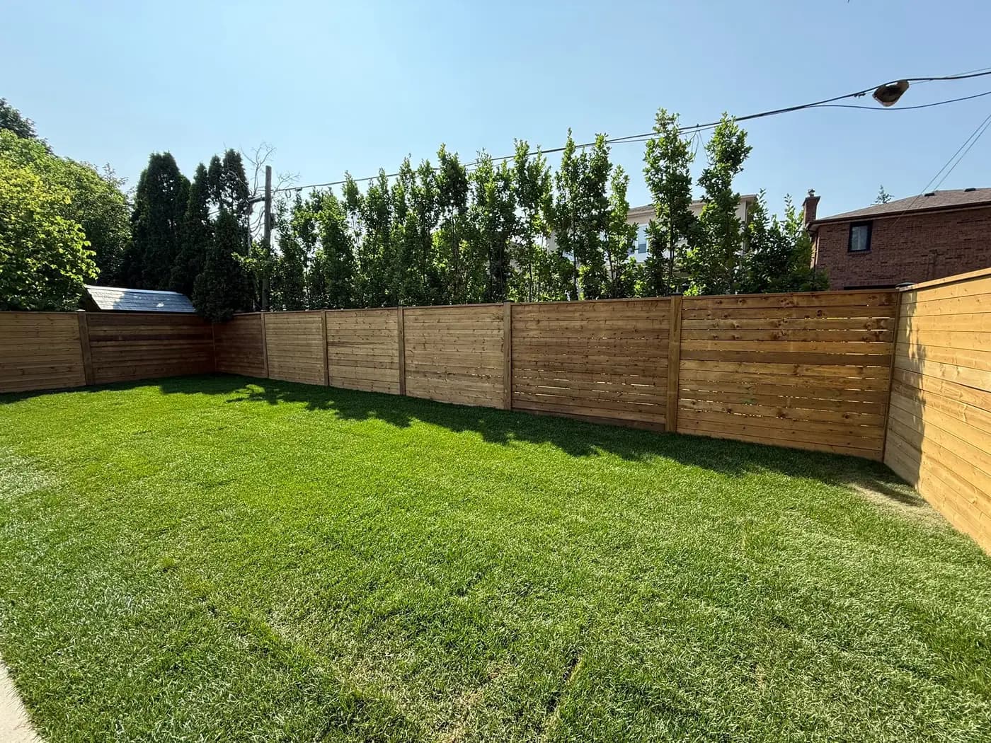 Horizontal wood board fence enclosing a back yard with established lawn and mature trees behind