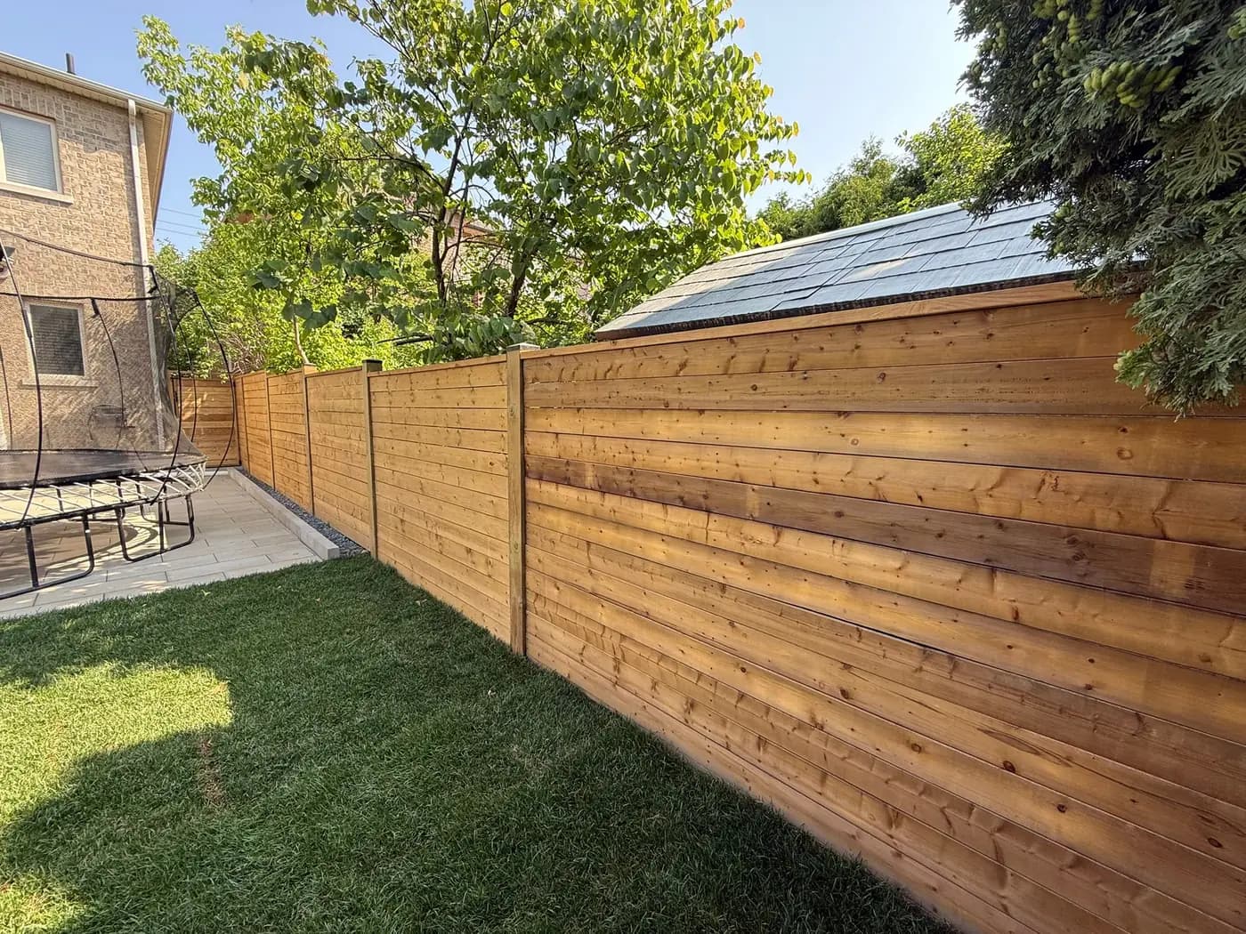 Horizontal wood fence meeting a paved patio area and lawn in a back yard