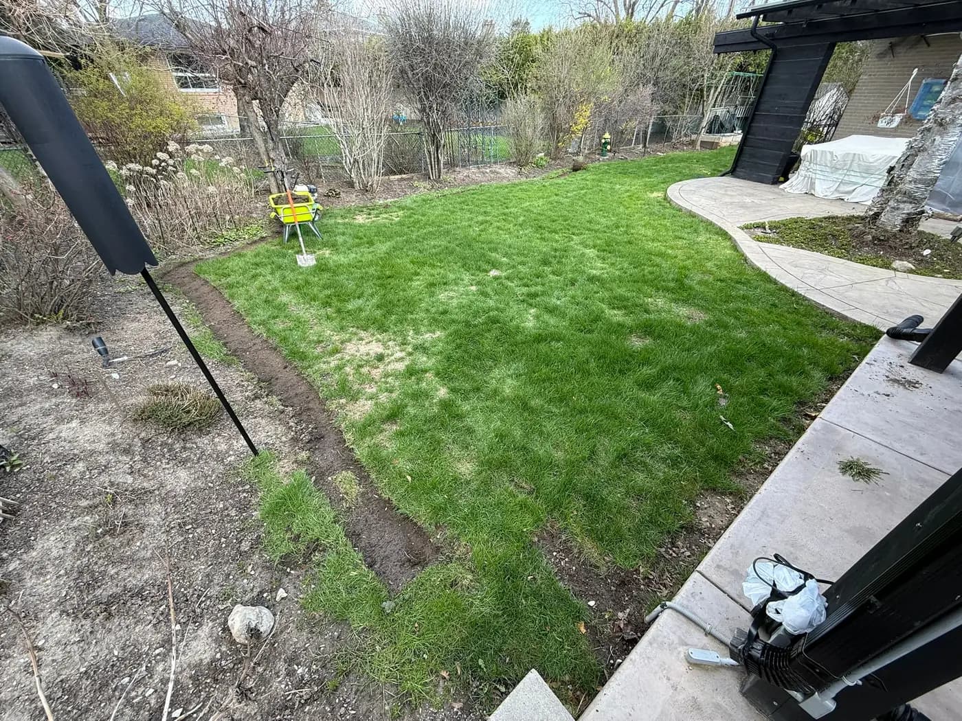 Rear yard left rough after construction, with compacted bare soil and patchy grass beside a curved walkway