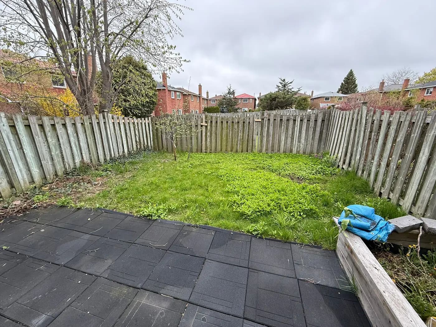 Enclosed back yard with mossy patchy ground and bare soil beside a dark paver patio